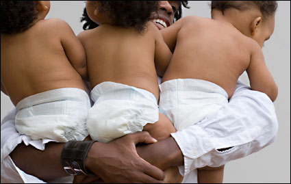 a father holding three babies in diapers