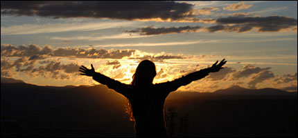 a woman with her arms spread wide against a setting sun