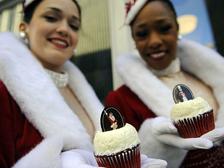 Two Rockettes display two Rockette Red Velvet cupcakes.