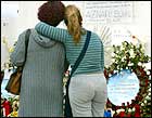 Two women embrace as they look at candles and flowers in front of Madrid's El Pozo railway station.