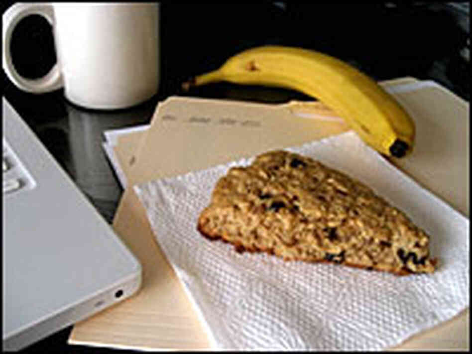 A scone is nestled on a napkin, completing a desktop breakfast with coffee and banana