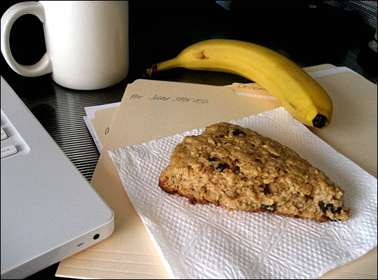 A scone is nestled on a napkin, completing a desktop breakfast with coffee and banana