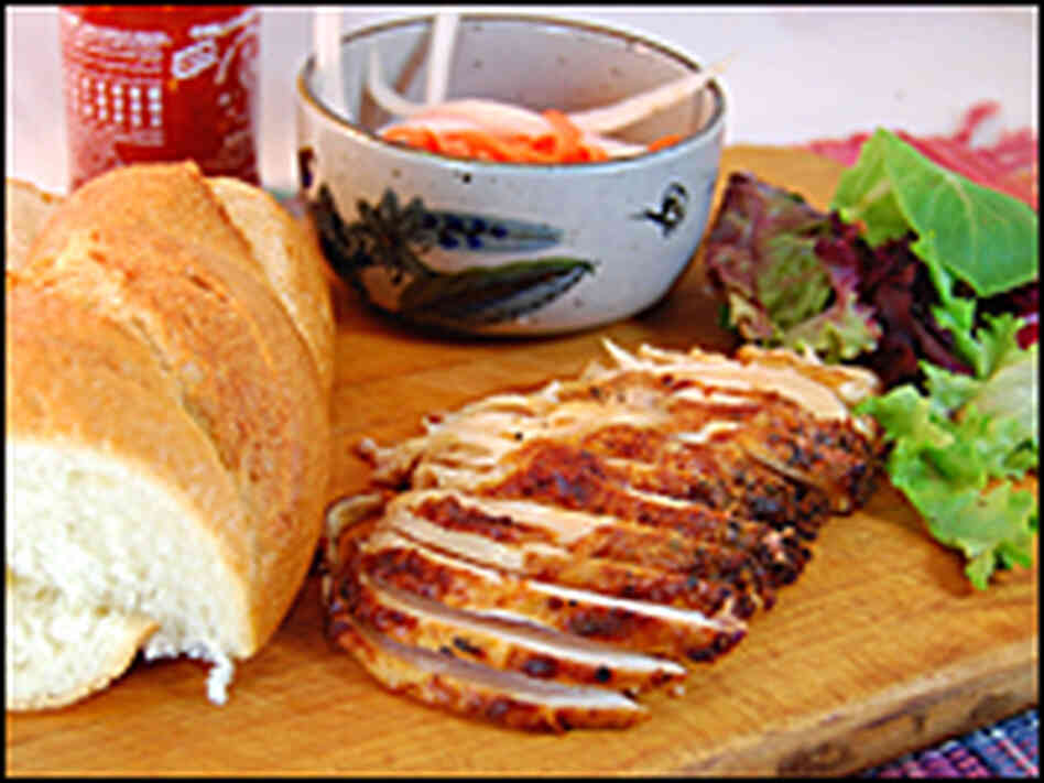Fixings for Banh Mi -- crusty bread, sliced meat, pickled radish, chili sauce -- on a cutting board
