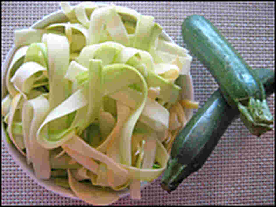 A bowl of squash ribbons sits with two whole green zucchini
