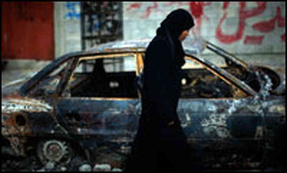A Palestinian woman walks past a burned car in northern Gaza, Jan. 19.