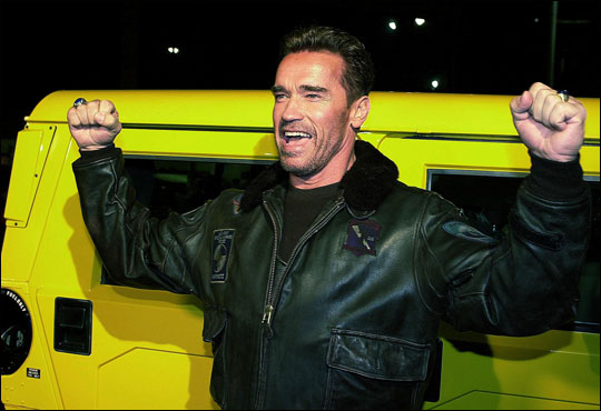 Arnold Schwarzenegger poses by his yellow Hummer
