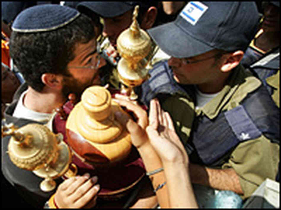 A Jewish settler carries the Torah in front of policemen surrounding a synagogue. A Jewish settler carries the Torah in front of policemen surrounding a synagogue.