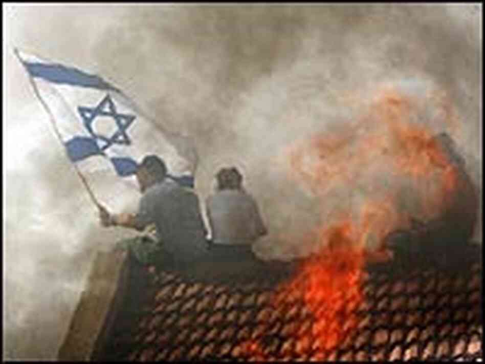 A Jewish settler waves an Israeli flag atop a burning roof in Gadid. A Jewish settler waves an Israeli flag atop a burning roof in Gadid.