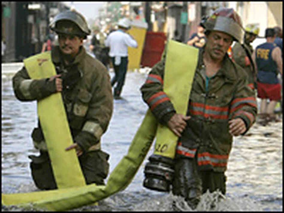 Firemen carry their hose through floodwaters to a burning looted retail store. Firemen carry their hose through floodwaters to a burning looted retail store.