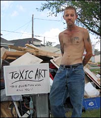 Jeffrey Holmes with discarded possessions; sign reads: 'Toxic Art: This Exhibition Will Kill You!'