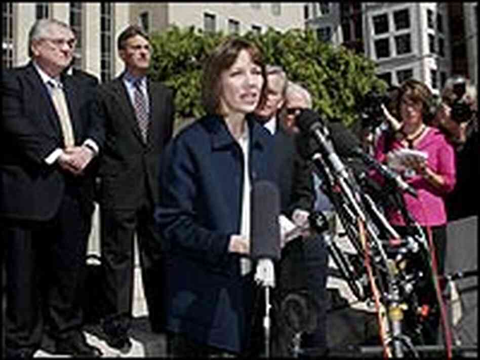 Judith Miller in front of a bank of microphones, surrounded by lawyers. Judith Miller in front of a bank of microphones, surrounded by lawyers.