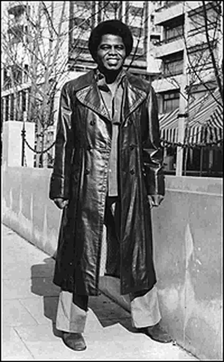 Brown stands on a street wearing a long leather coat.