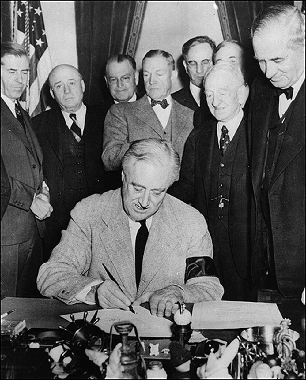 FDR signs a declaration of war as members of Congress look on.