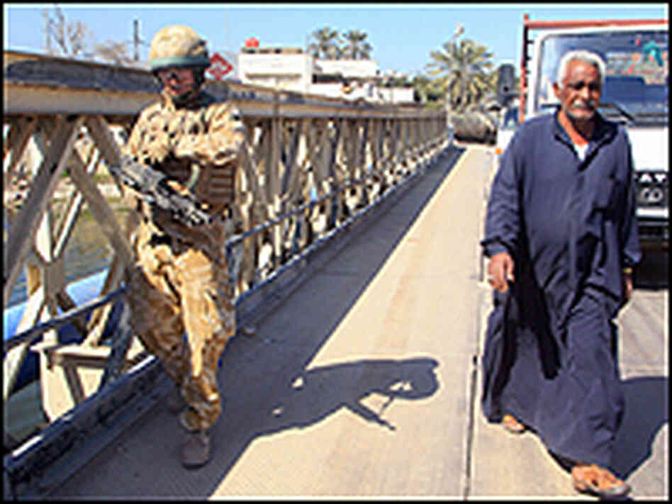 A British soldier patrols in Basra, walking alongside a local citizen.