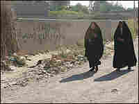 Women, required to wear an abaya, walk past a spray-painted wall. Women, required to wear an abaya, walk past a spray-painted wall.