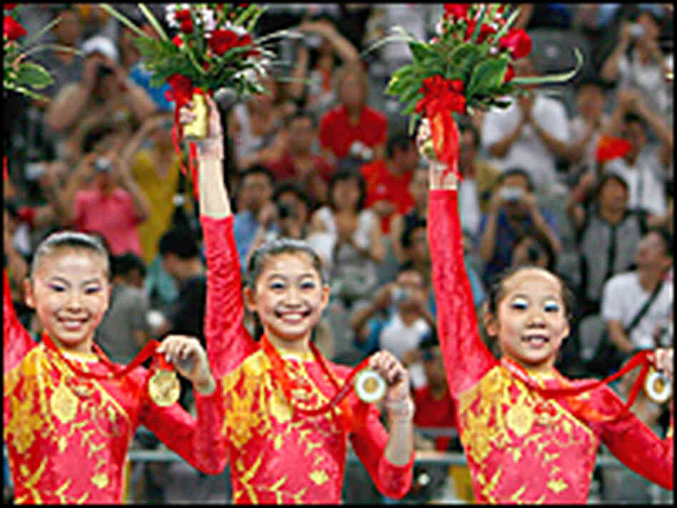 Members of China's women's gymnastics team hold up their gold medals and bouquets after their win