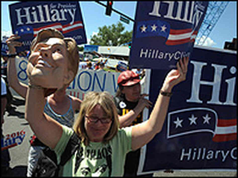 A protester holds up a Hillary sign and a rubber mask of Hillary Clinton.