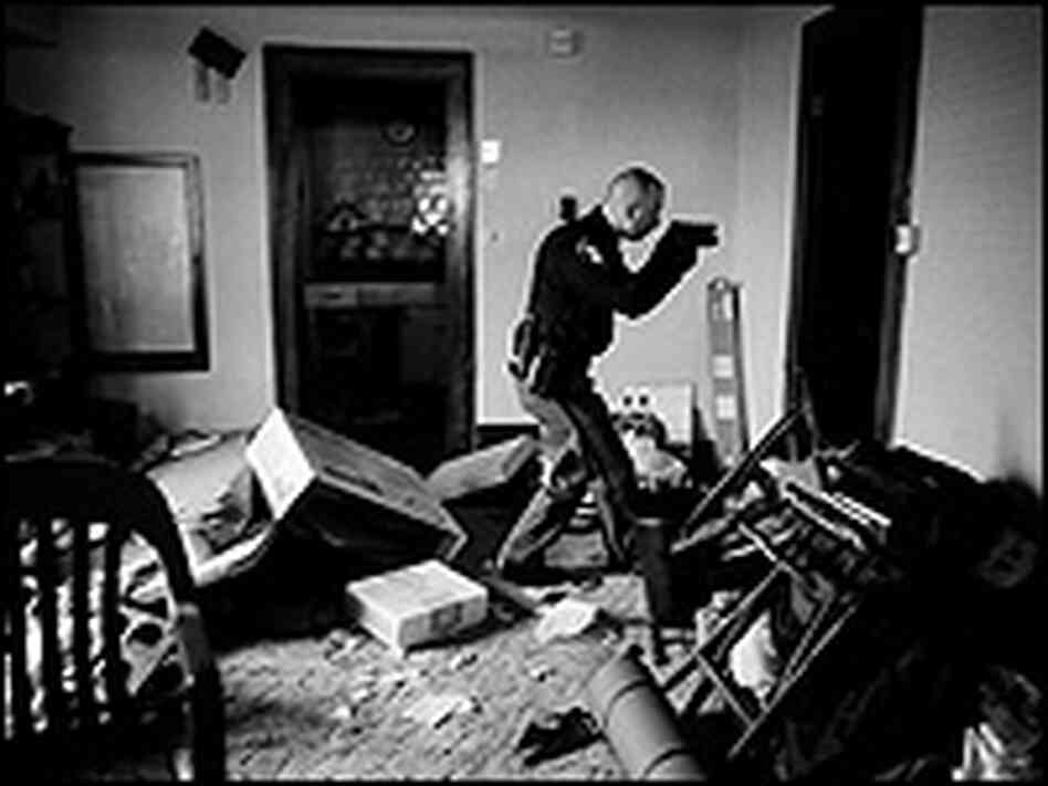 A police officer with gun drawn secures a foreclosed home.
