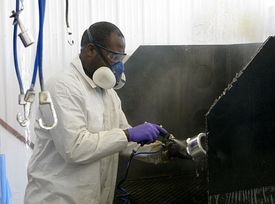 Larry Harbour of Broken Bow, Neb., sprays chrome plating on plastic wheel caps in his detail shop.