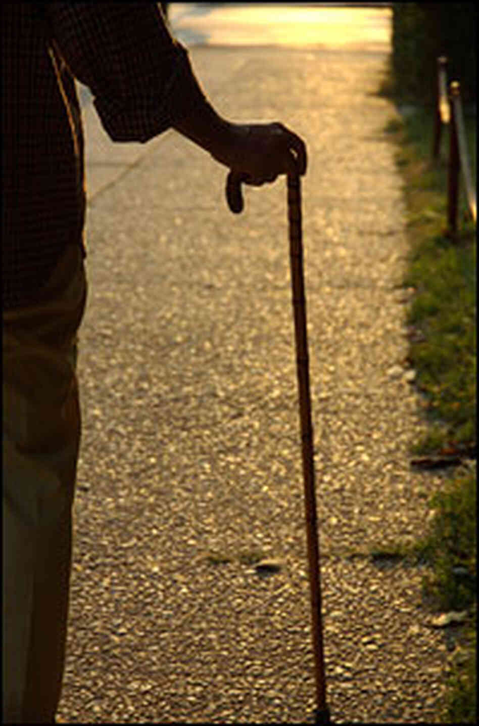 Detail of an elderly person's hand on a cane, with a street visible in the foreground. Detail of an elderly person's hand on a cane, with a street visible in the foreground.