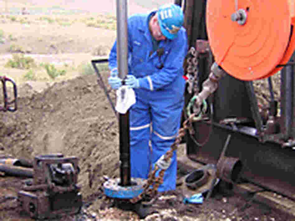 A worker wipes oil off the coring tool as it comes up from the earth. A worker wipes oil off the coring tool as it comes up from the earth.