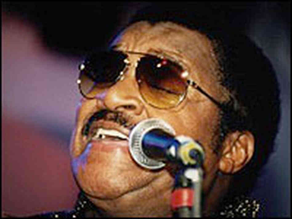 Little Milton, in dark shades, sings into a microphone. Little Milton, in dark shades, sings into a microphone.