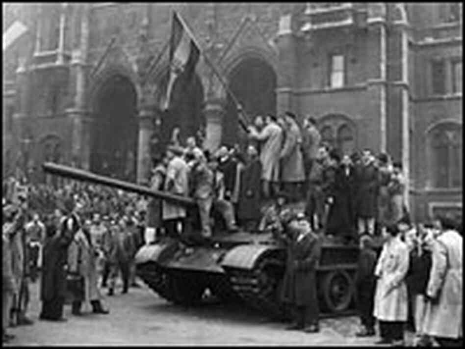 A group of men hold a flag on top of a tank in front of the Parliament building during the Hungarian