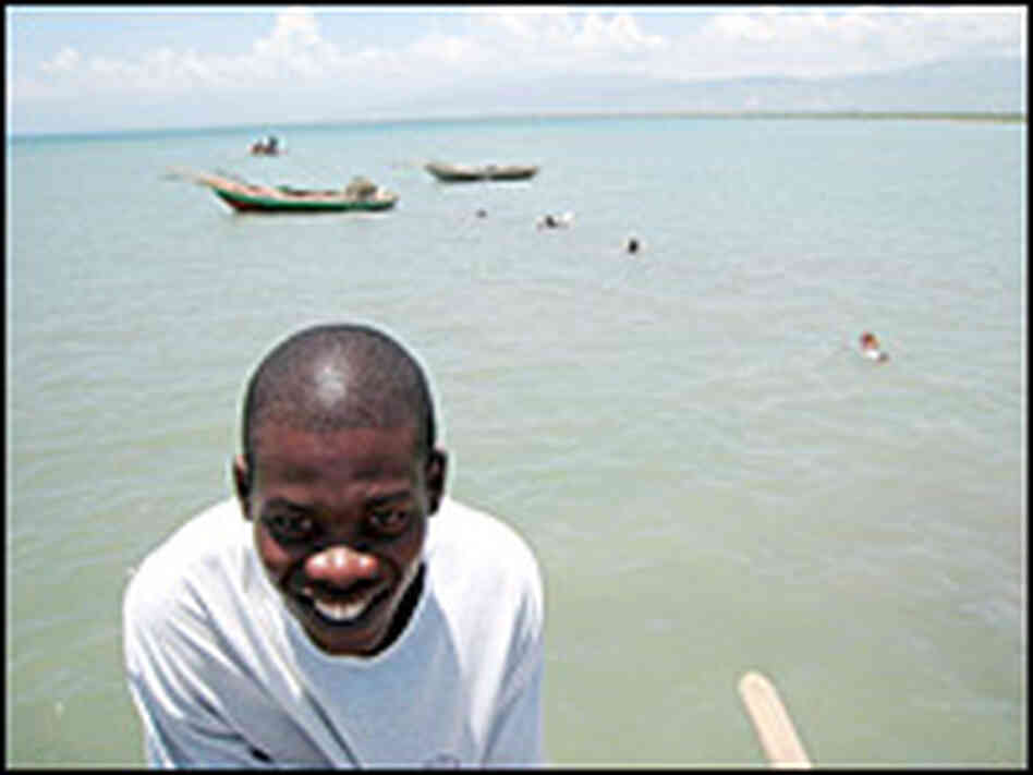 A young man laughs as children swim next to a pier in Cite Soleil.