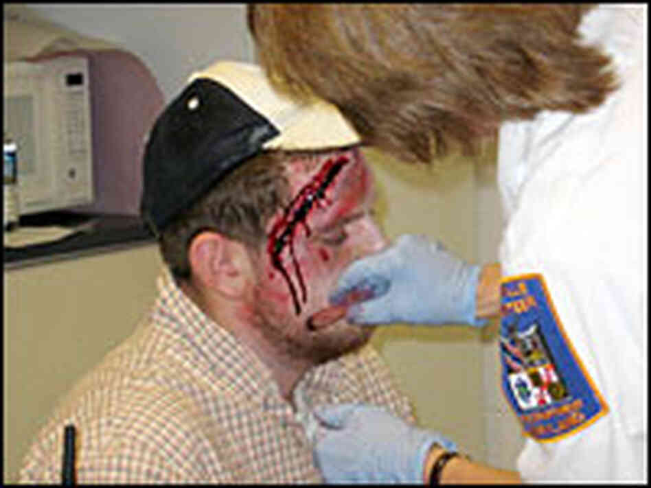 Capt.  Peggy Miller applies makeup to senior Travis Blair to create injuries