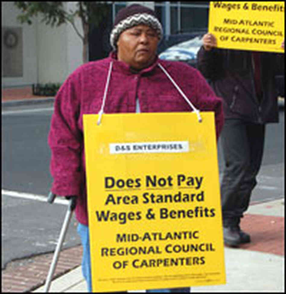 A woman pickets on behalf of the carpenter's union for $8 an hour.