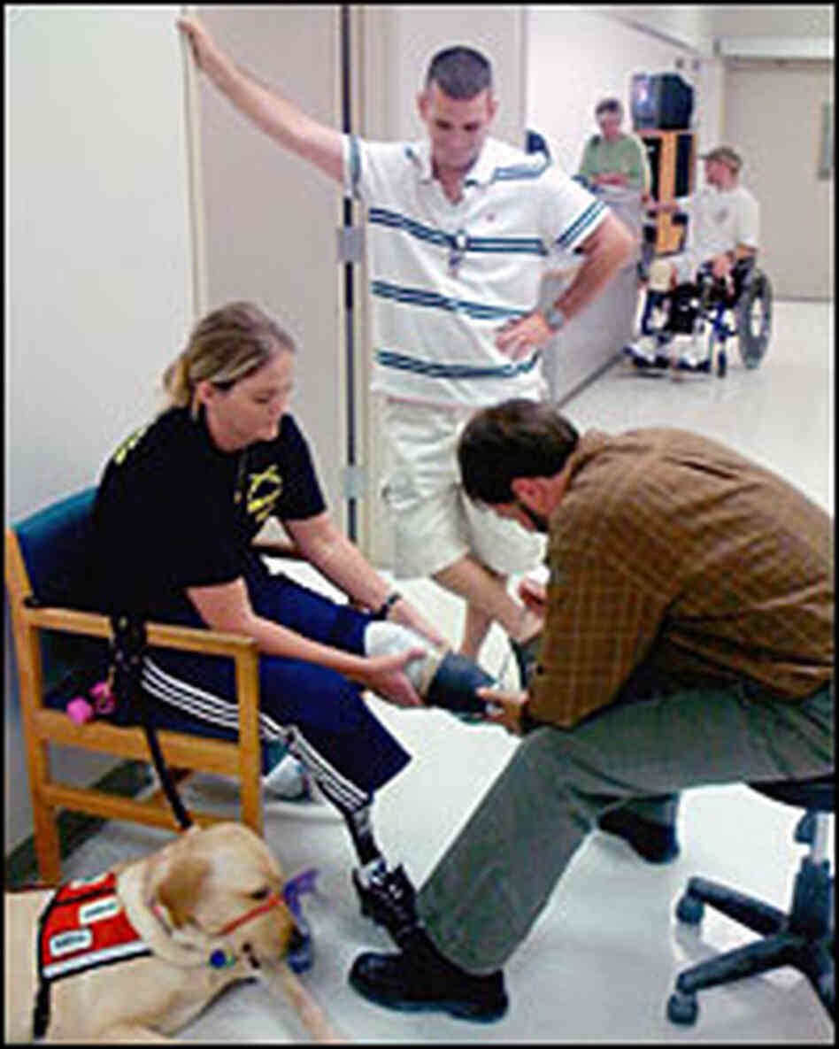 Sue Downes' husband, Gabe, looks on as prosthetist David Beachler adjusts her prosthetic leg.