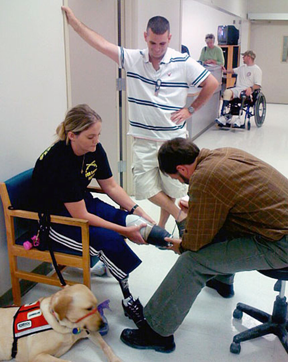 Sue Downes' husband, Gabe, looks on as prosthetist David Beachler adjusts her prosthetic leg.