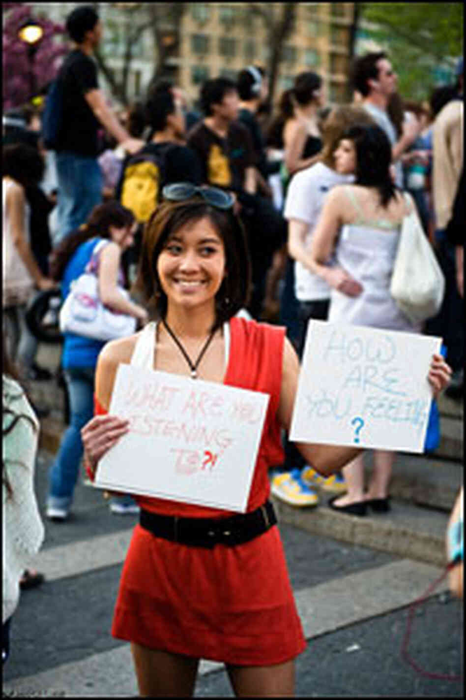 A woman holds signs saying "What are you listening to?" and "How are you feeling?" at a silent rave.