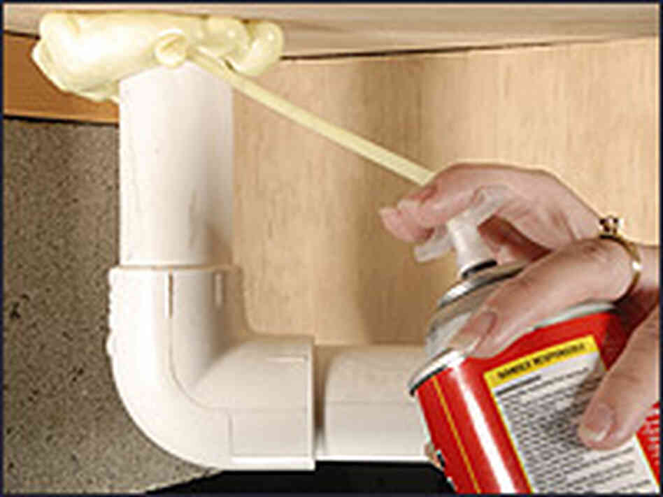 A homeowner sprays foam insulate around the base of a pipe. A homeowner sprays foam insulate around the base of a pipe.