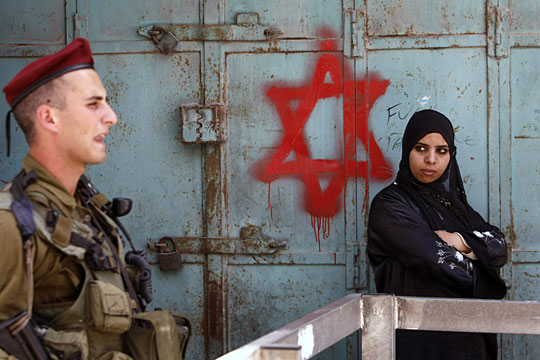 An Israeli soldier stands guard near a Palestinian woman in Hebron.