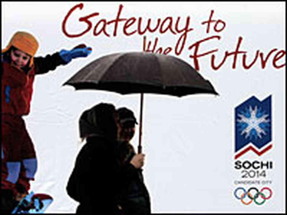 A couple walks in front of a poster for the 2014 Winter Olympics in Sochi, Russia.