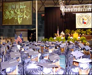 Soldiers in Baghdad are seen on a video screen listening to a graduation ceremony via satellite as Shoemaker High School seniors await the awarding of their diplomas in central Texas; Photo: Todd Martin, Killeen (Texas) ISD