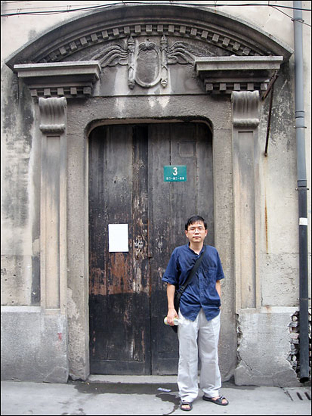 Shu stands outside the door of the house where he grew up.