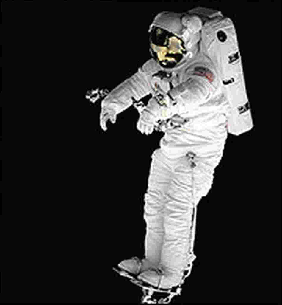 Against the blackness of space, mission specialist Peter J.K. Wisoff stands on a robot arm.