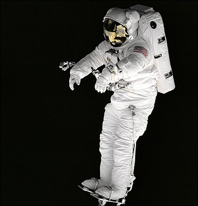 Against the blackness of space, mission specialist Peter J.K. Wisoff stands on a robot arm.