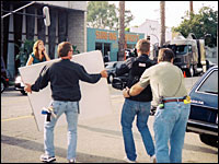 Dagg (from the back, right) guides the camera operator backwards as he films Mandy Moore (left) walking across a busy street in Venice, Calif.  