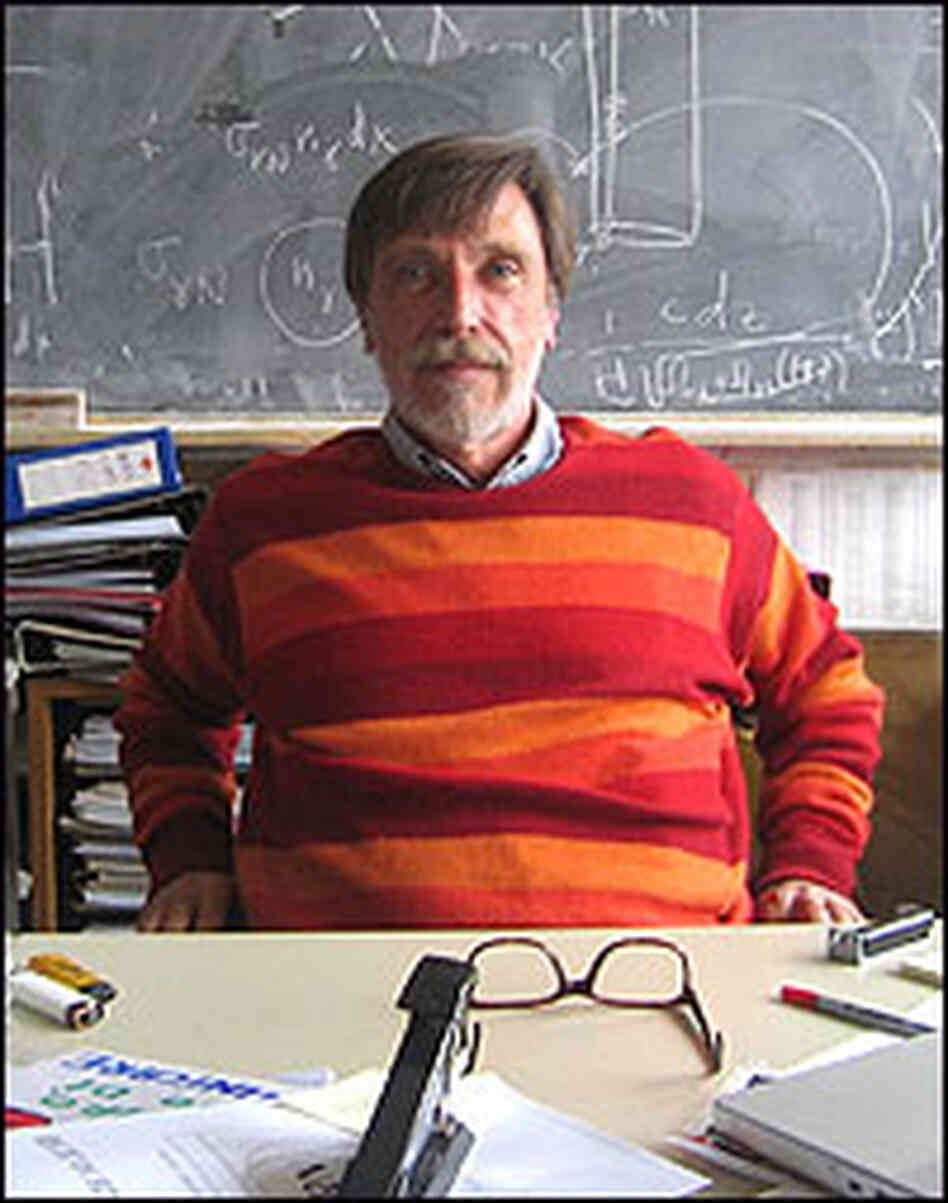 Physicist Alvaro De Rujula sits in his messy office in front of a blackboard.