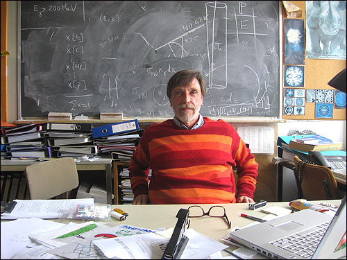 Physicist Alvaro De Rujula sits in his messy office in front of a blackboard.