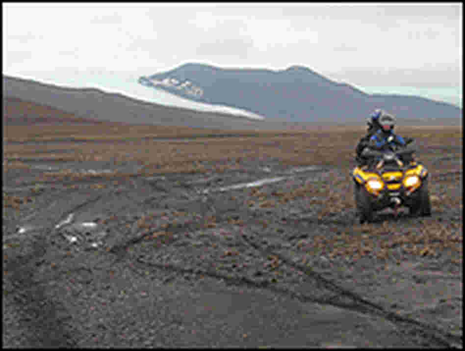 An ATV drives across the rocky desert in front of the Hofsjokull glacier.