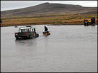 An ATV driver attaches a chain to an expedition truck stuck in a river. An ATV driver attaches a chain to an expedition truck stuck in a river.
