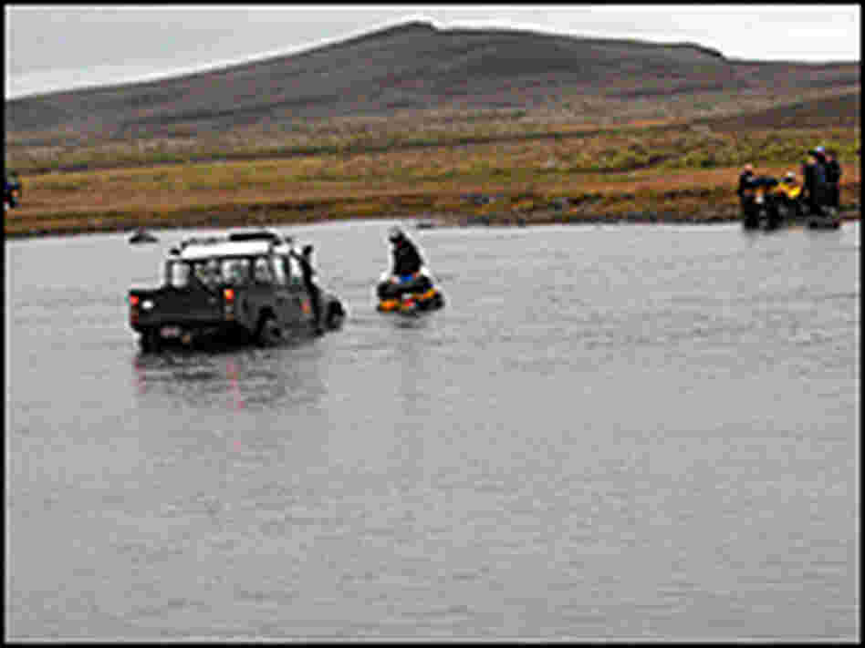 An ATV driver attaches a chain to an expedition truck stuck in a river.