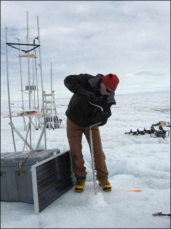 Ian Joughin uses an ice drill to sink a pole into the surface.
