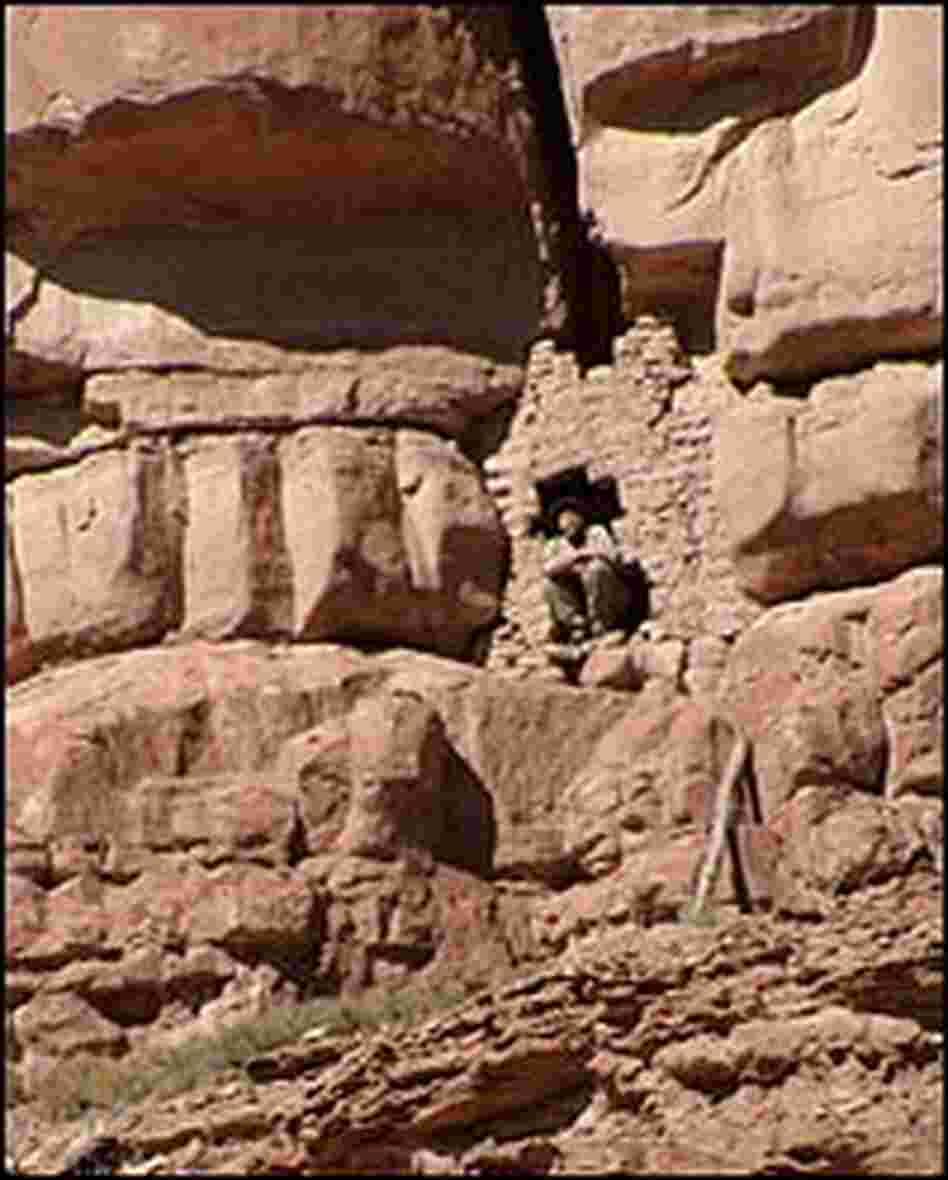 Craig Childs crouches in the doorway of a cliff dwelling.