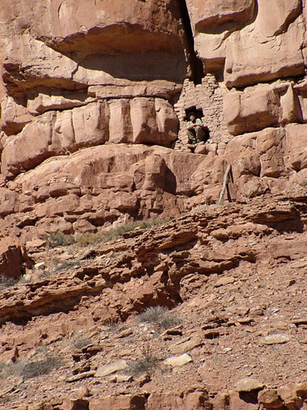 Craig Childs crouches in the doorway of a cliff dwelling.