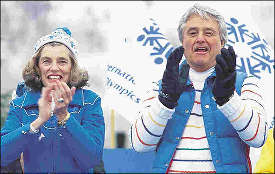 Shriver and her husband, wearing matching blue coats, applaud athletes at the Special Olympics.